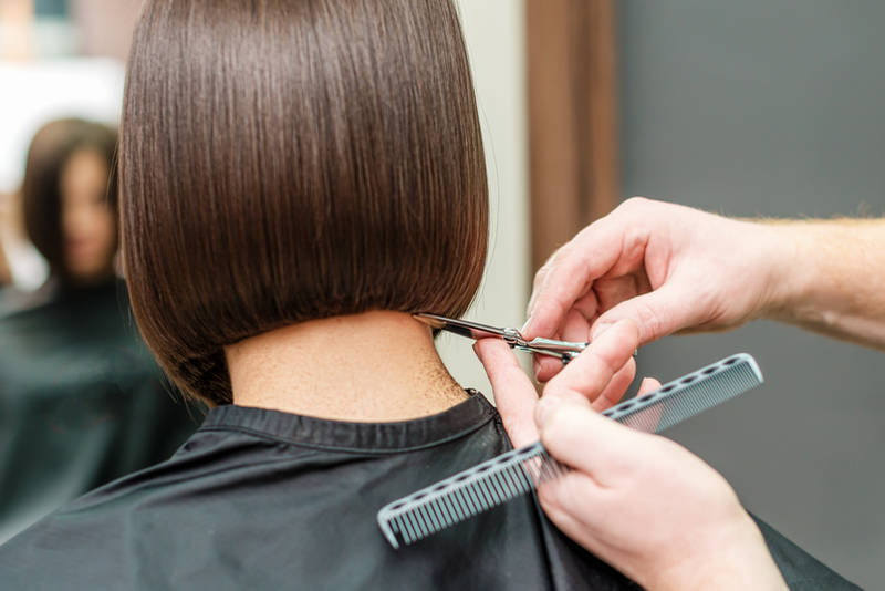 Hands of professional hair stylist is cutting hair tips with scissors and comb.